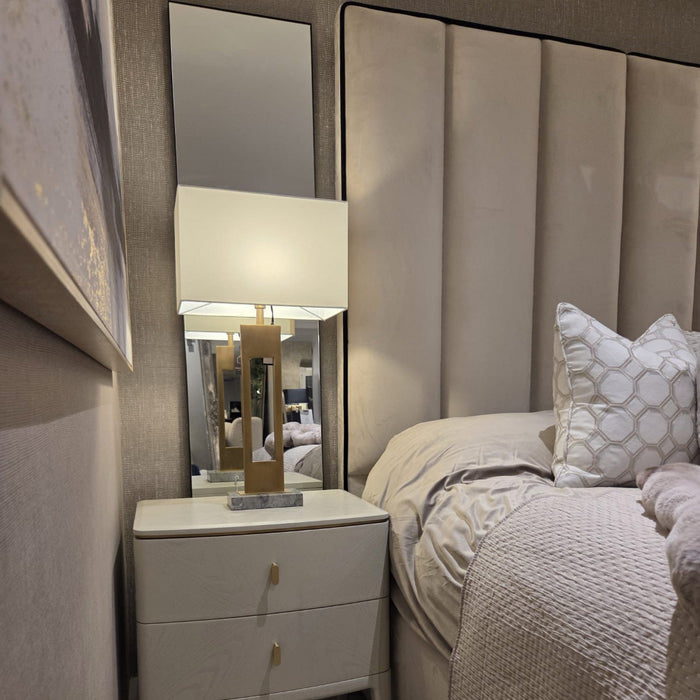 Custom Belle bed with a tall upholstered panel headboard, beige bedding, and a matching nightstand with lamp.